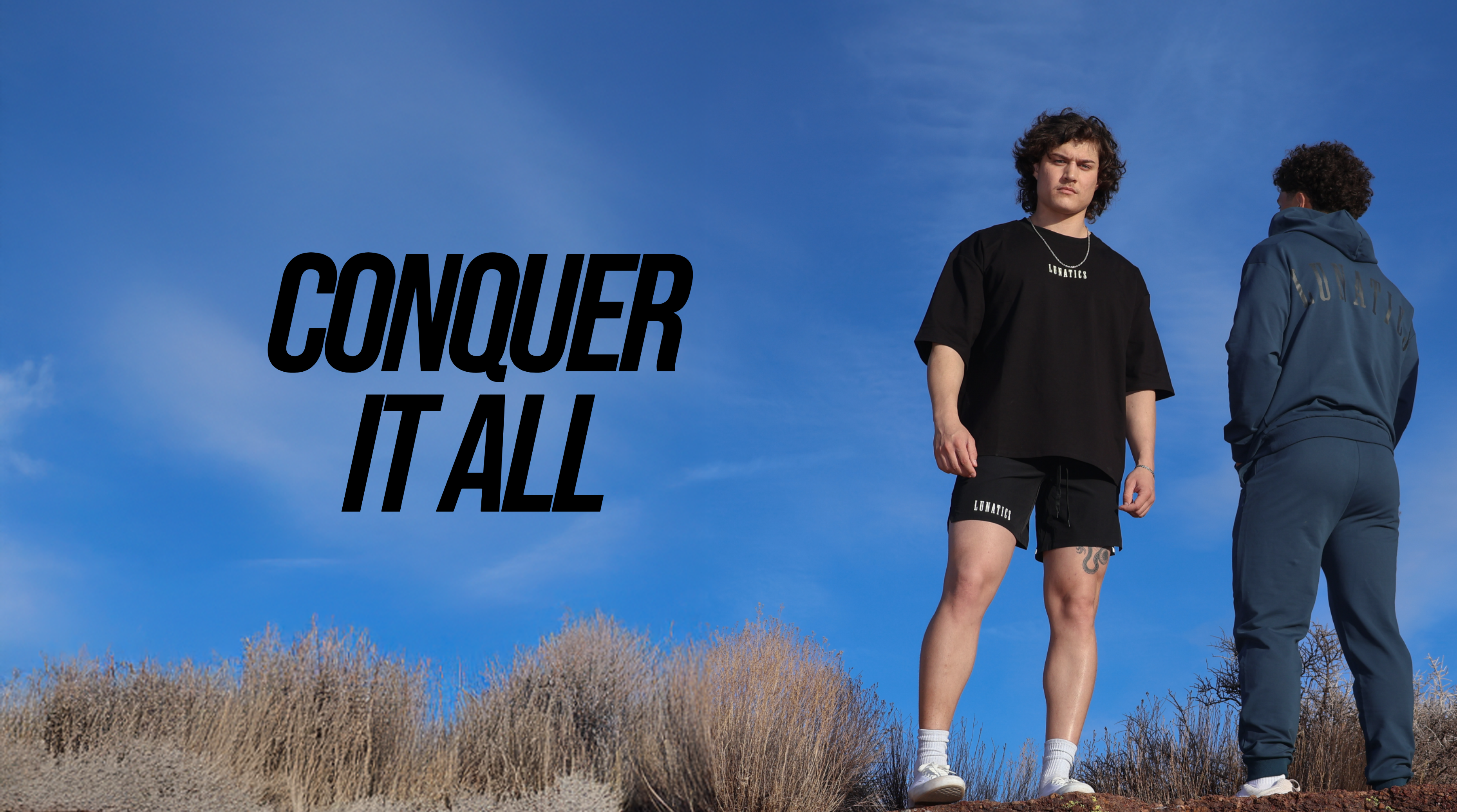 Three people standing on a rocky outcrop with 'Conquer It All' text against a blue sky.